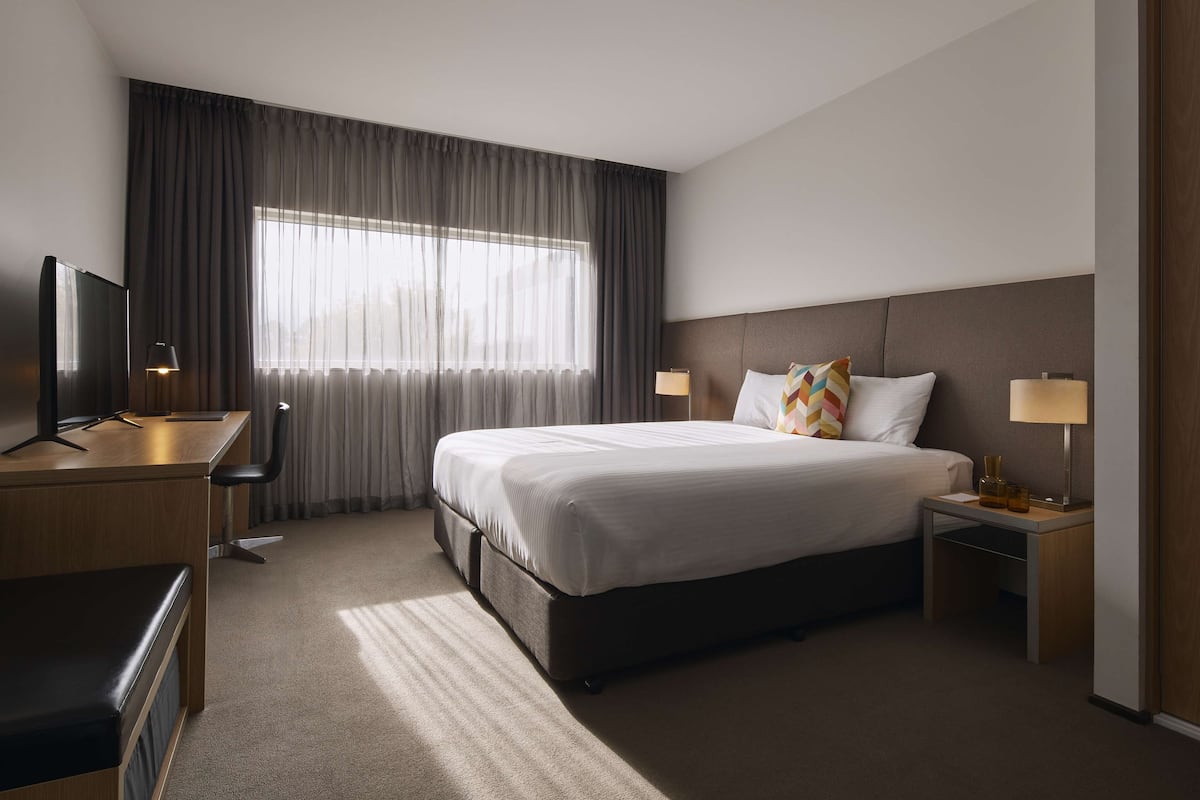 Habitación de hotel con una cama grande, un escritorio con silla, dos mesitas de noche con lámparas y un televisor en el escritorio.