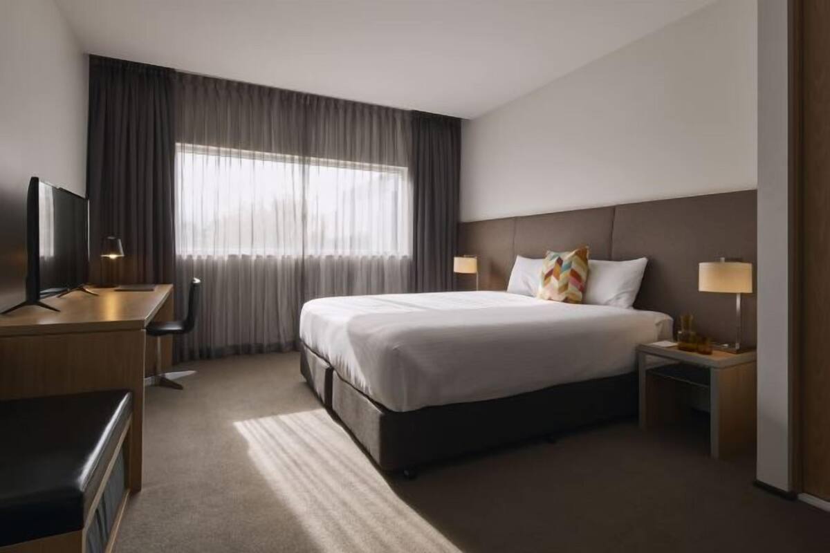 Una habitación de hotel con cama, escritorio, televisor y dos lámparas de noche.