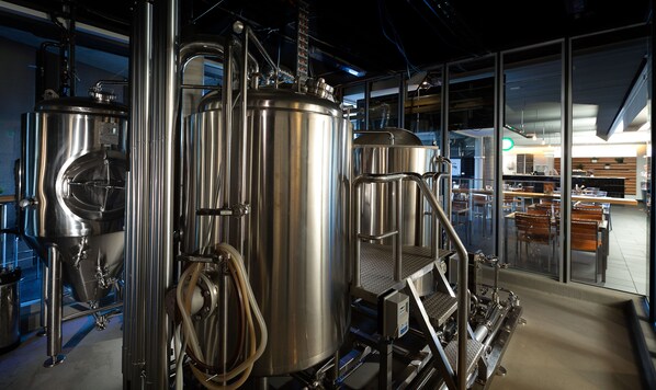 A modern industrial kitchen with stainless steel equipment and a seating area visible through glass walls.