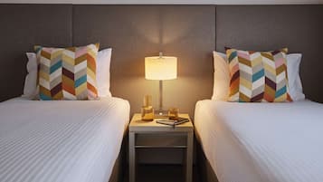 Ein Hotelzimmer mit zwei Betten, jedes mit einem gemusterten Kopfkissen, einem Nachttisch mit Lampe und einer Flasche.