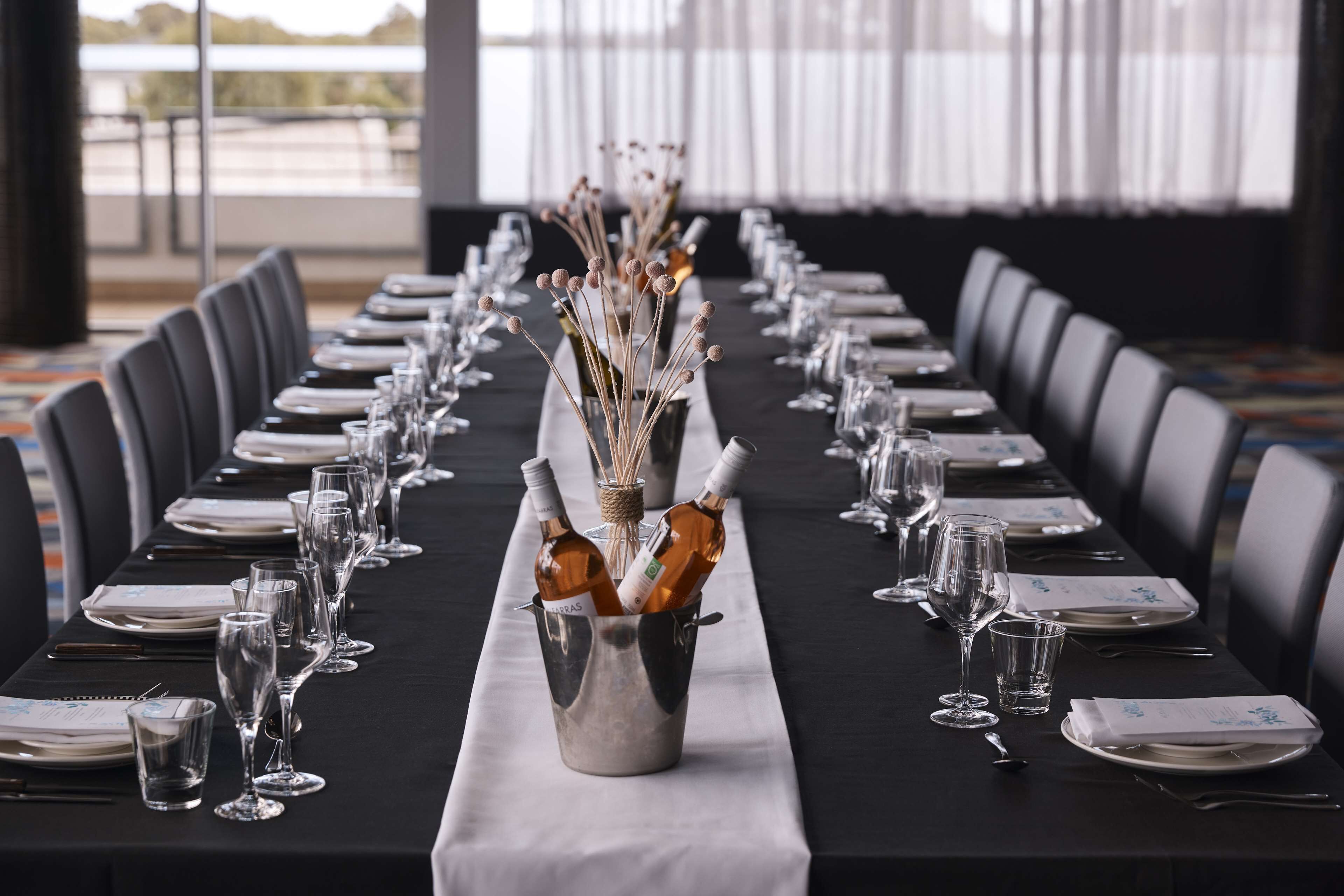 A long table set for a formal event with a central vase of flowers, wine bottles, and neatly arranged plates and glasses.