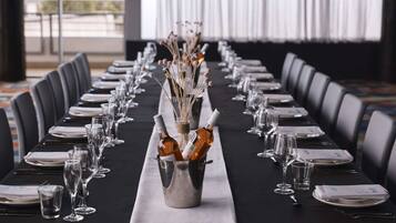 A long table set for a formal event with a central vase of flowers, wine bottles, and neatly arranged plates and glasses.