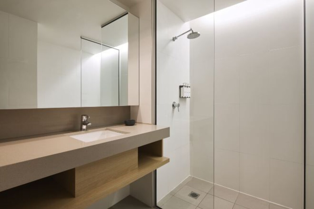 A modern bathroom with a large mirror, a sink, and a shower.