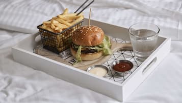 A tray with a burger, fries, and drinks on a bed.
