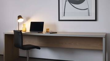 A modern workspace with a desk, laptop, and chair, featuring a framed artwork on the wall.