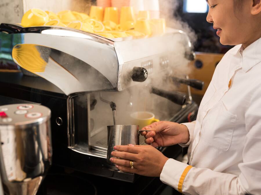 Una persona operando una máquina de café, sosteniendo una taza de metal.