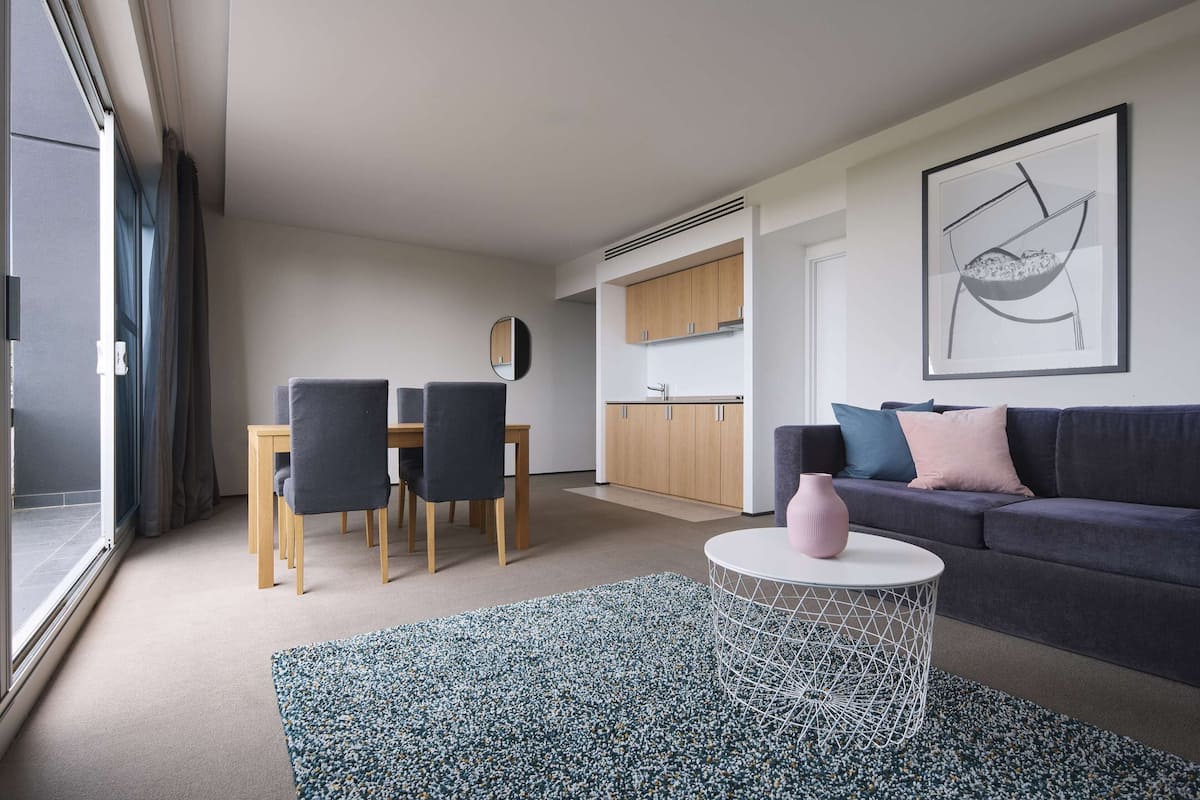 Una sala de estar moderna con un sofá, una mesa de comedor con sillas, una zona de cocina y un ventanal grande.