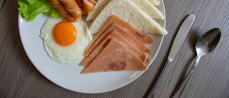 A plate with a fried egg, ham, sausages, and bread on a table.