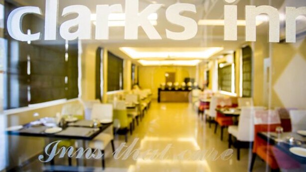 A hotel interior with a long corridor, tables, and chairs arranged for dining. - Clarks Inn Nehru Place (New Delhi)