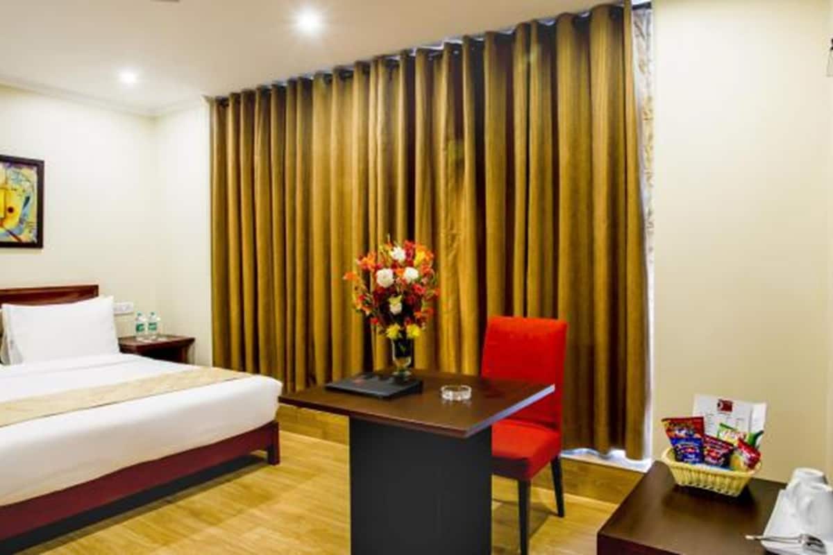 Una habitació d'hotel amb un llit, un escriptori, una cadira, un vas de flors i un quadre a la paret.