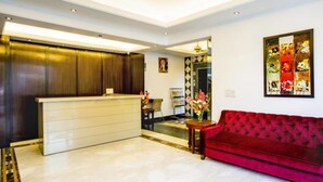 A modern living room with a red velvet sofa, a wooden reception desk, and a patterned wall. - Clarks Inn Nehru Place (New Delhi)