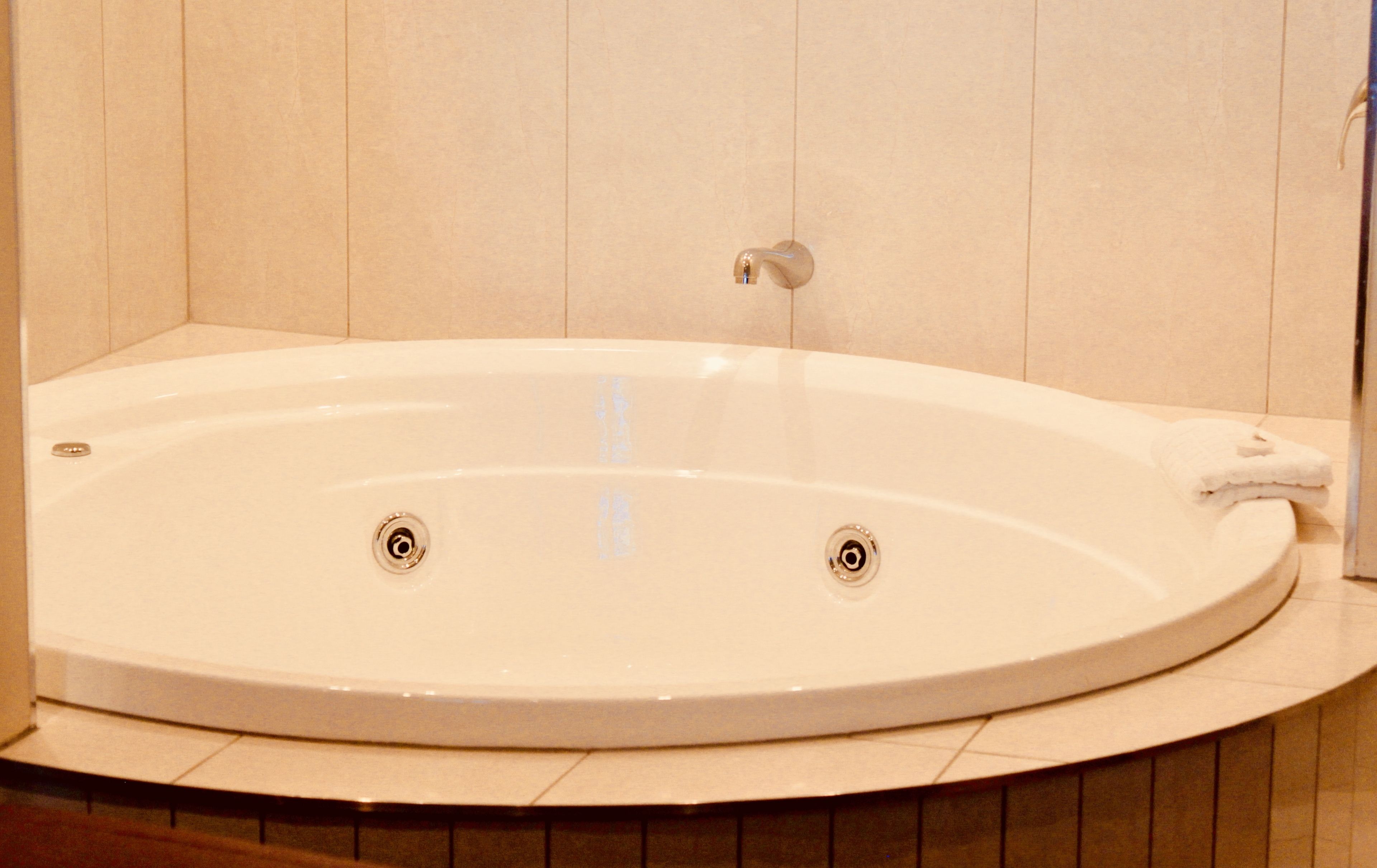 A large, oval-shaped bathtub with two faucets, set against a tiled wall.
