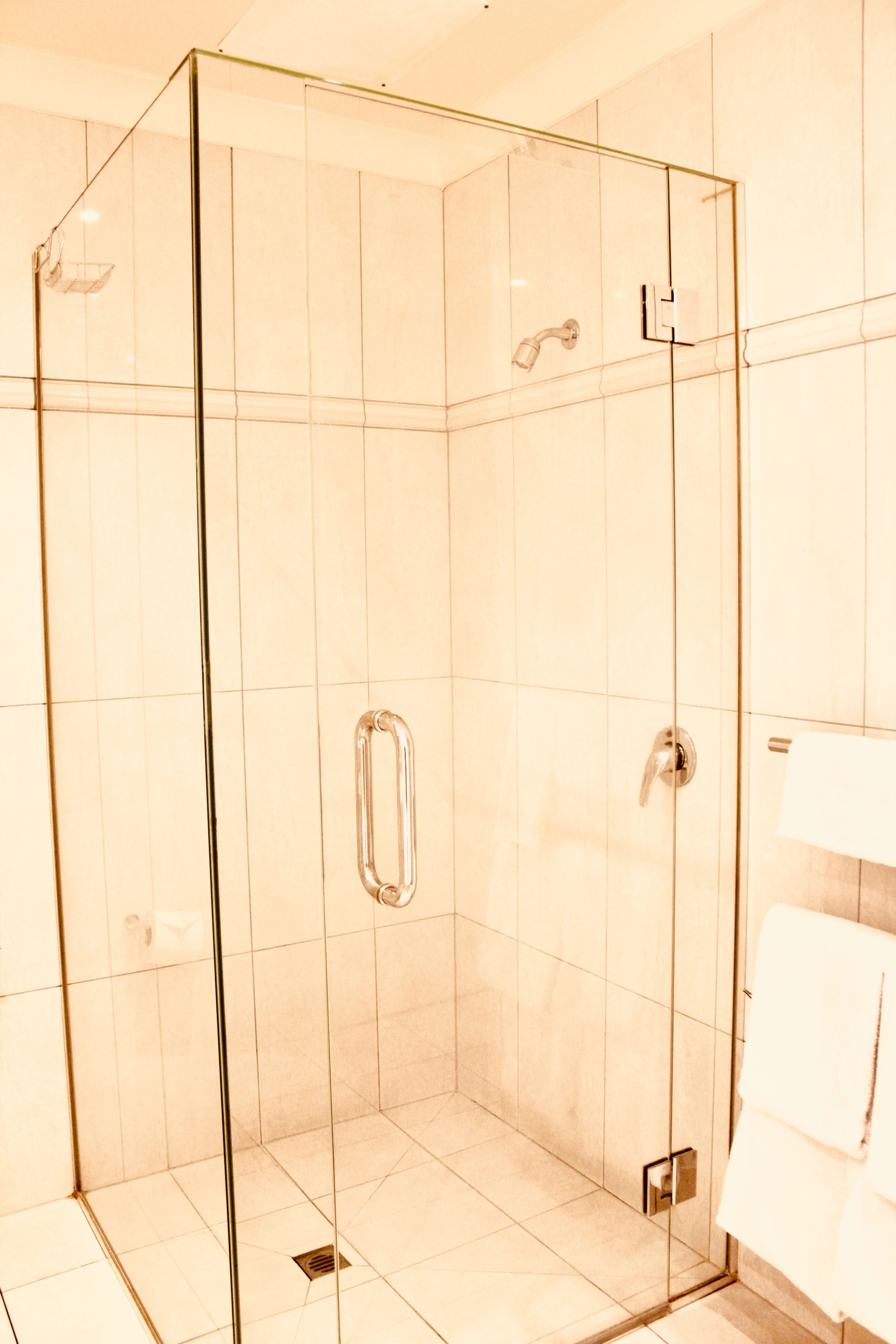 Ducha con mampara de vidrio, cabezal de ducha manual, toallero y desagüe visible.
