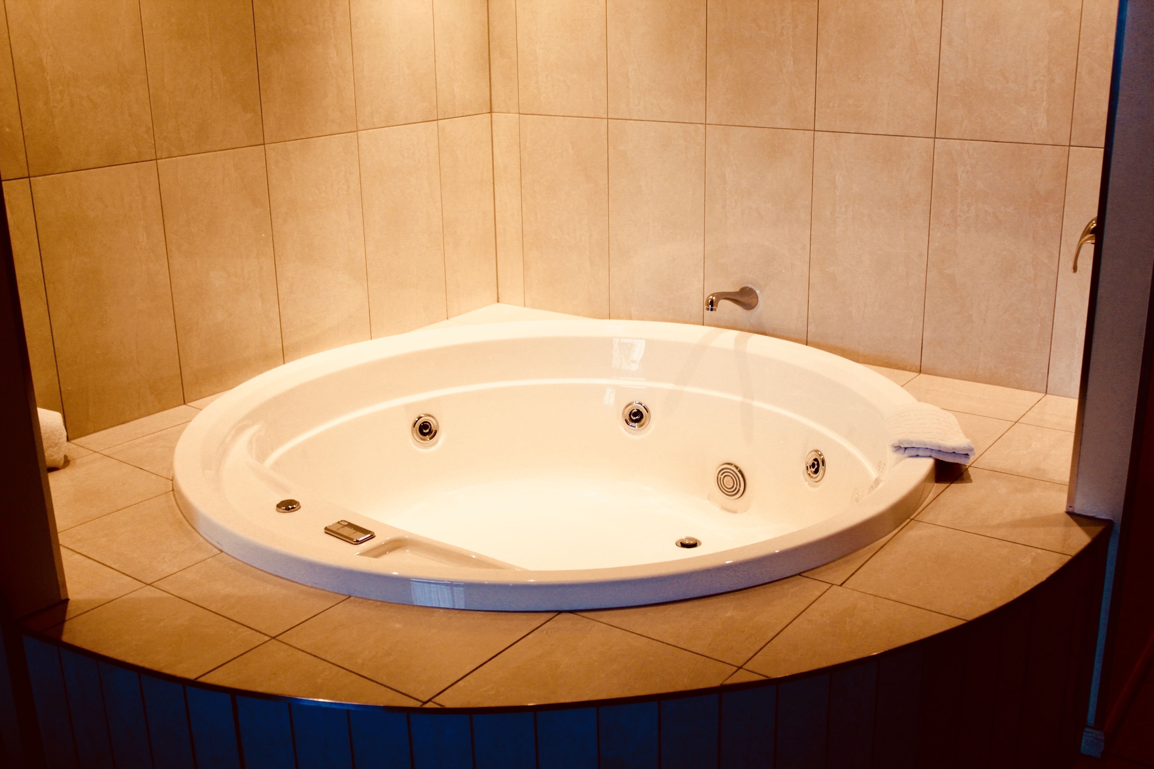 A large, round, freestanding bathtub in a bathroom with beige tiles on the walls and floor.