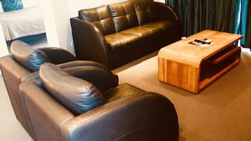 A living room with a brown leather sofa, a wooden coffee table, and a dark curtain in the background.