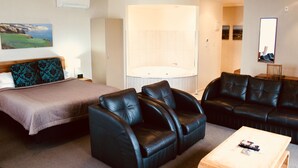 Hotellihuone, jossa on sänky, kaksi nahkaista nojatuolia, puinen sohvapöytä, suuri peili ja poreallas.