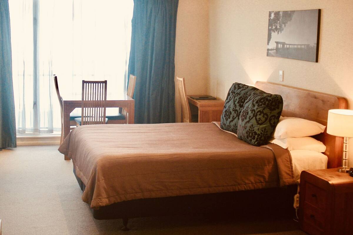 Habitación de hotel con cama, escritorio, silla y vistas al exterior.