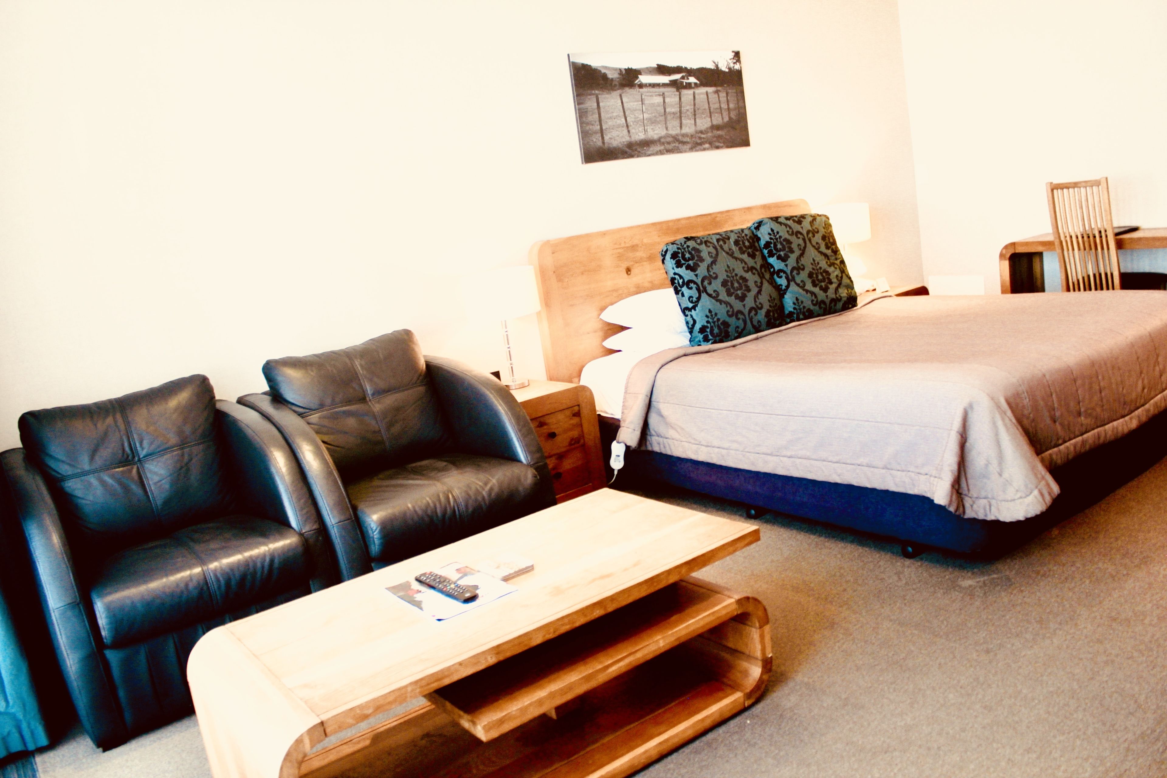 Une chambre à coucher avec un lit, deux fauteuils en cuir noir, une table basse en bois et une table de chevet avec une lampe.