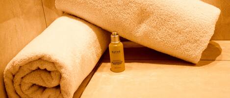 A bathroom with a wooden floor, a rolled white towel, and a bottle of Bath & Body Works rejuvenating body wash.