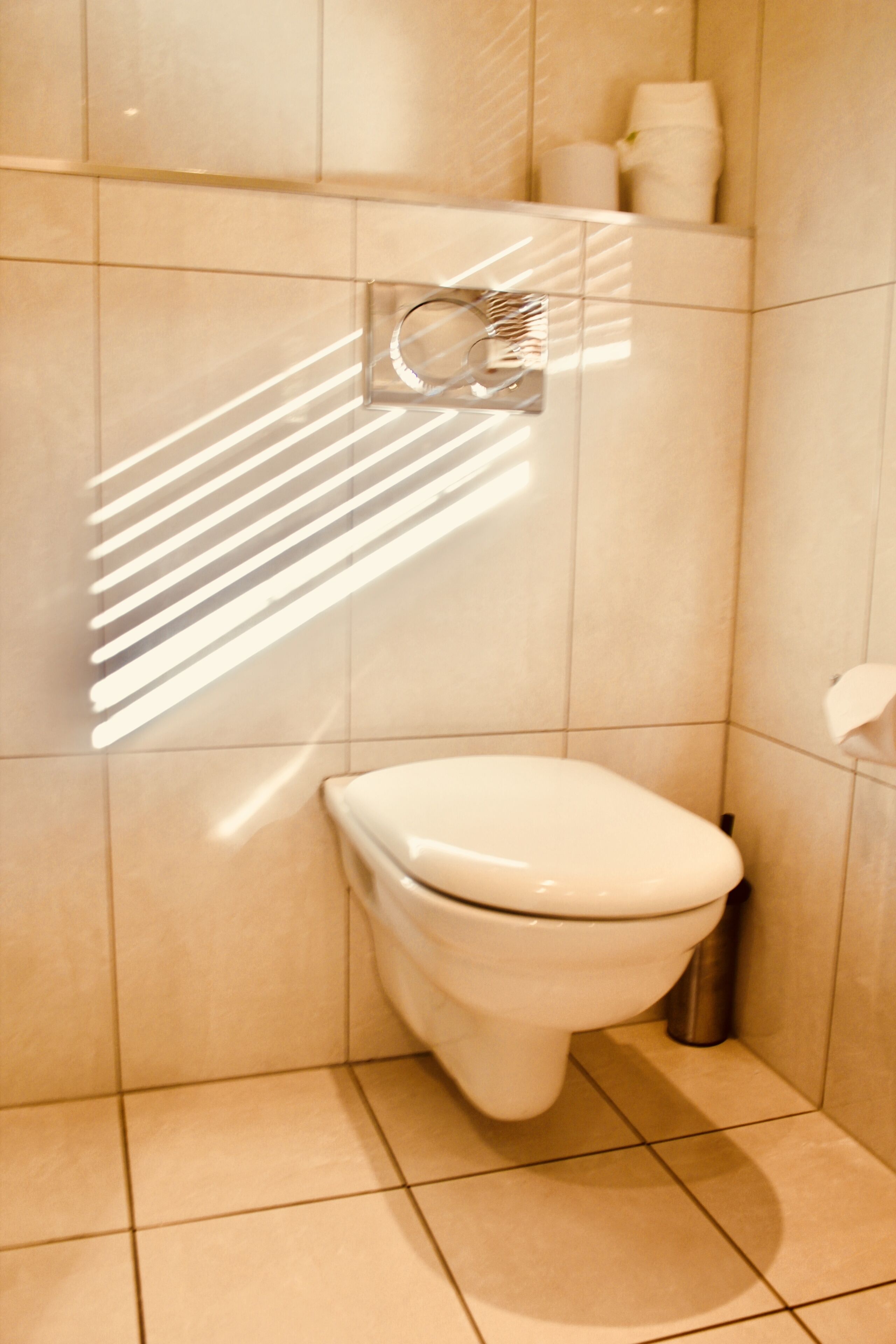 A modern bathroom with a toilet, a hand dryer, and a toilet paper holder on the wall.