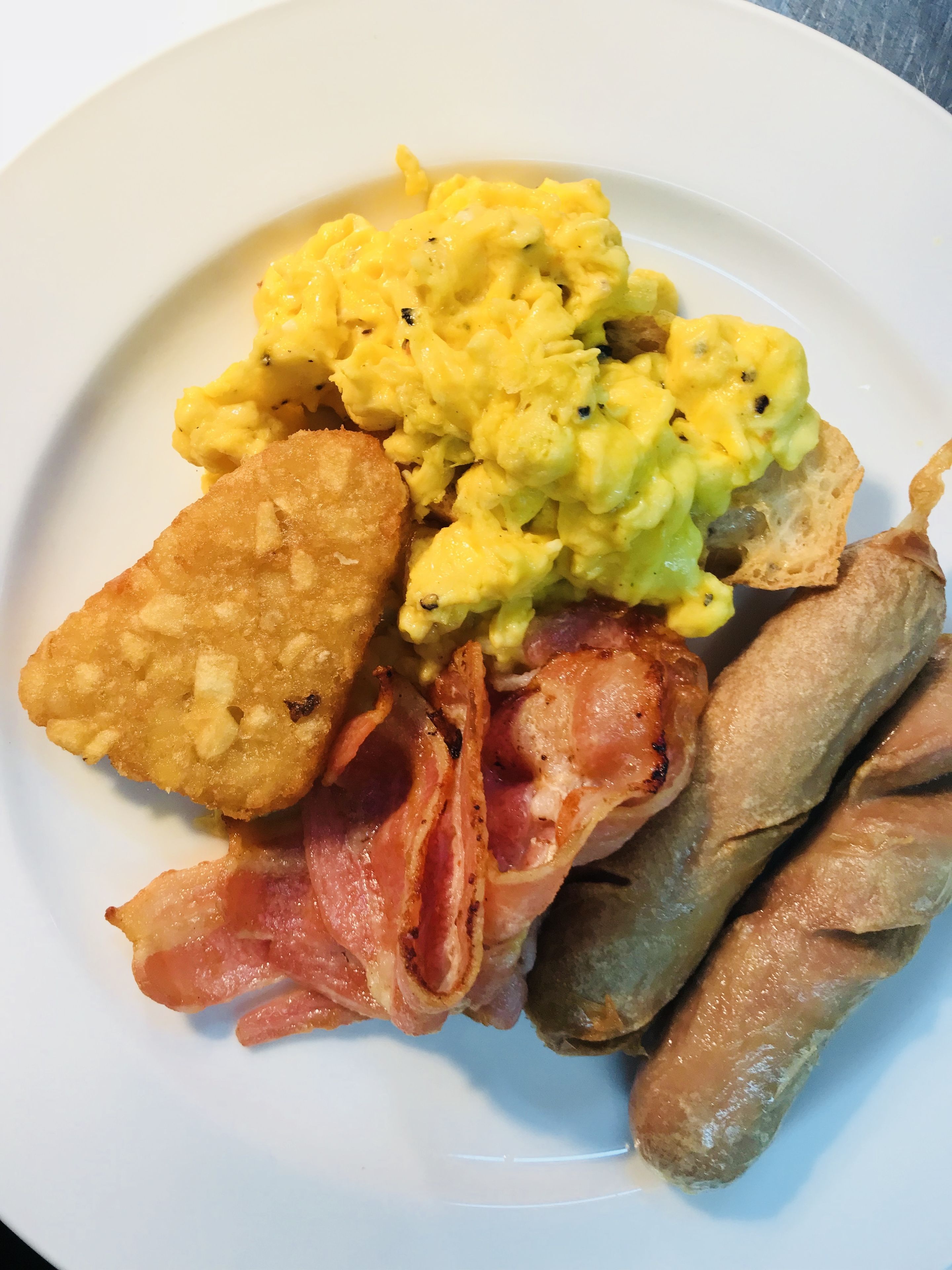 A plate with scrambled eggs, fried potatoes, bacon, and sausages.
