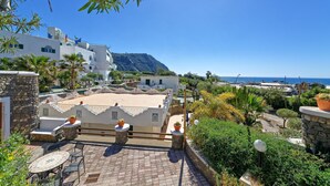 Terraço no telhado com vista para o mar, rodeado por vegetação e edifícios brancos.