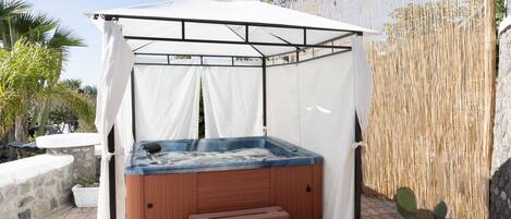 A hot tub under a white canopy, surrounded by a stone wall and potted plants.
