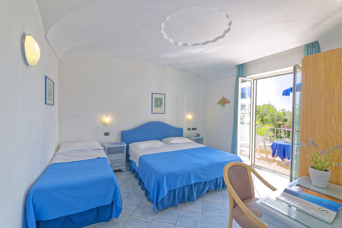 A hotel room with two beds, a desk, a chair, and a balcony with a view.