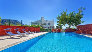 Piscina com espreguiçadeiras e um edifício ao fundo.