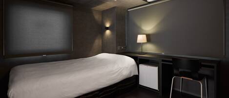 A modern hotel room with a bed, desk, chair, and a wall-mounted lamp.