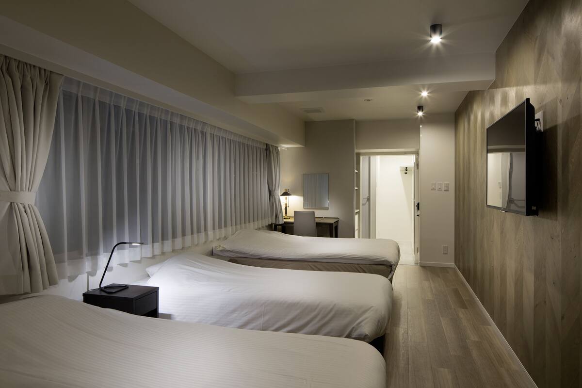 A hotel room with two beds, a desk, a chair, a TV, and a large window with curtains.