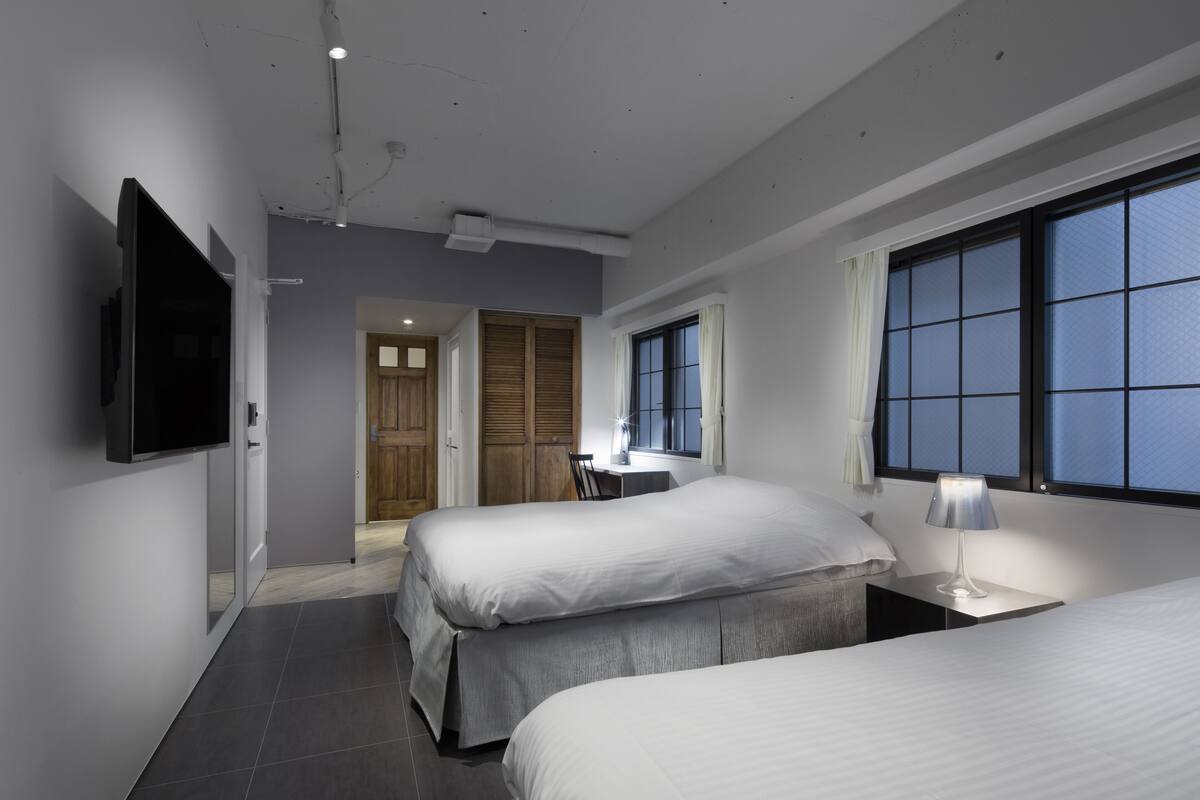 A modern hotel room with two beds, a desk, and a TV mounted on the wall.