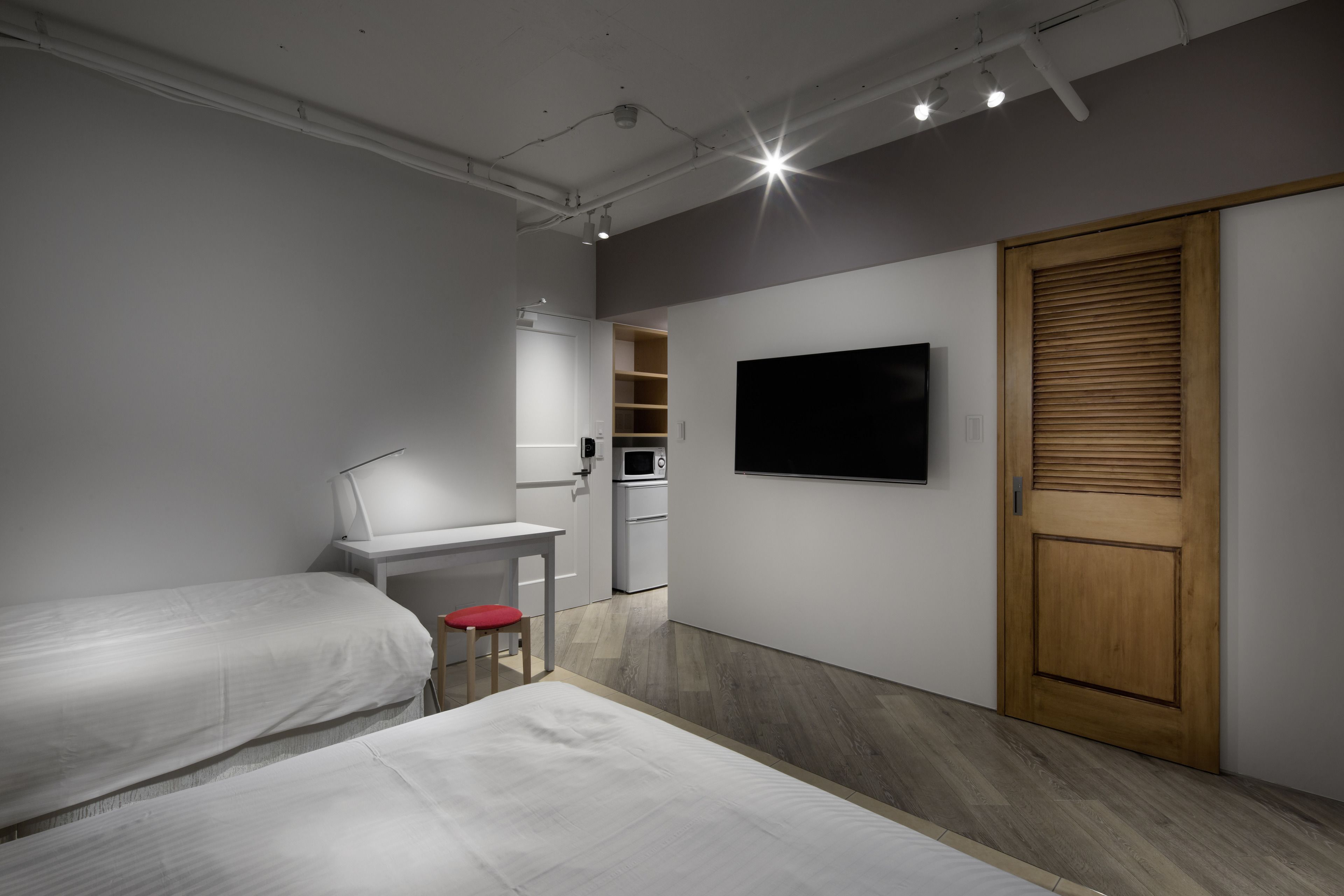 A compact bedroom with two beds, a desk, a television, and a wardrobe.