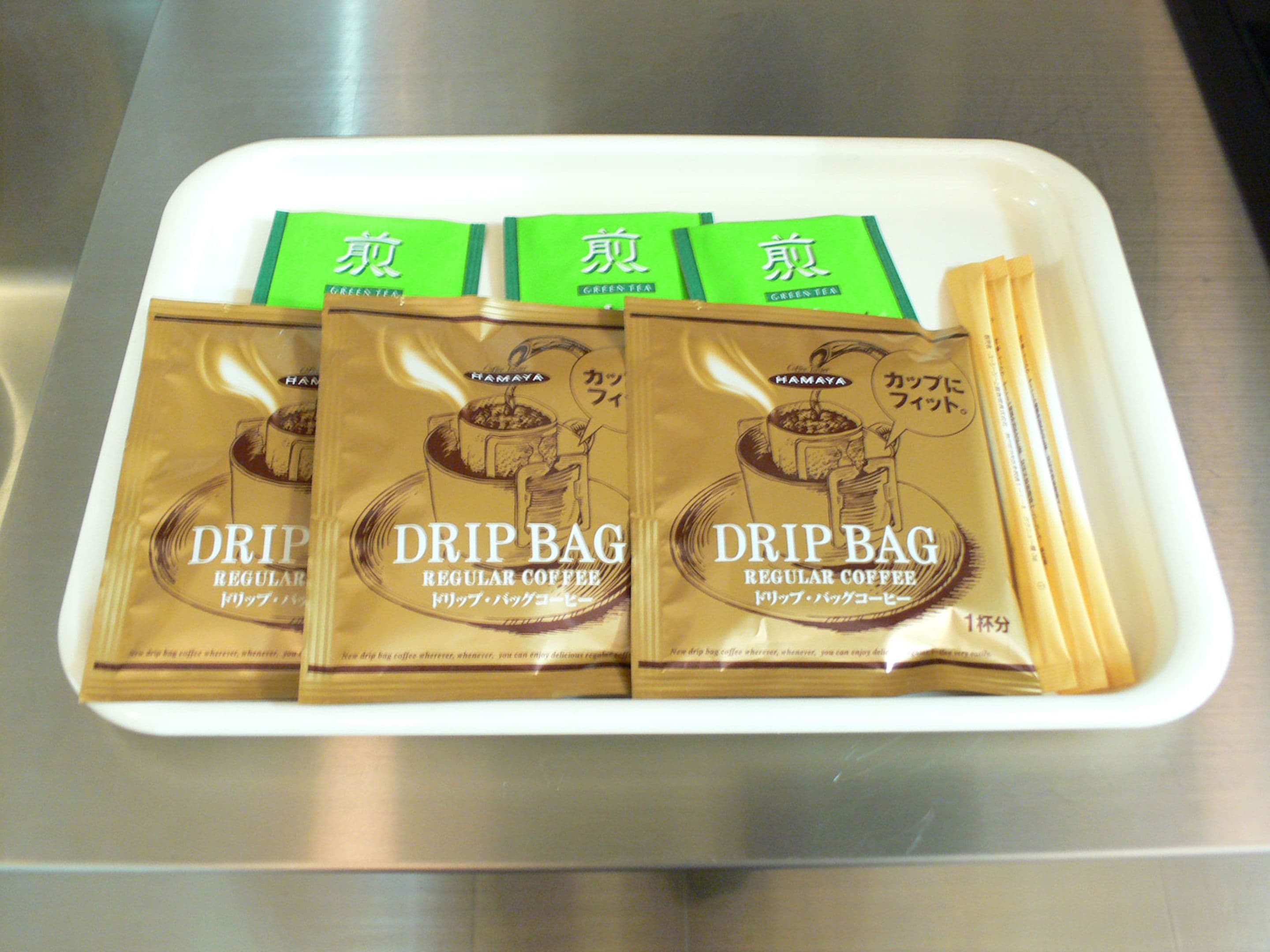 A tray with four drip coffee bags and a green box.