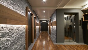 A hallway with a wooden floor, stone walls, and doors leading to rooms. - City Hotel N.U.T.S. (Tokyo)