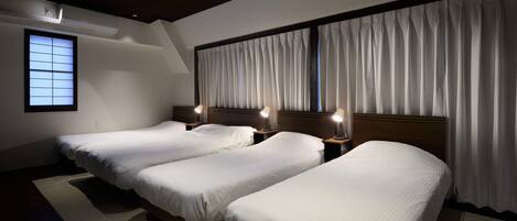 A hotel room with three single beds, a large window with curtains, and a wooden ceiling.