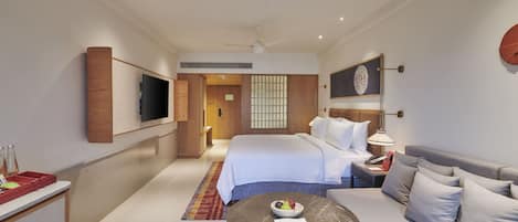 A modern hotel room with a bed, a sofa, a dining table, and a TV on the wall.