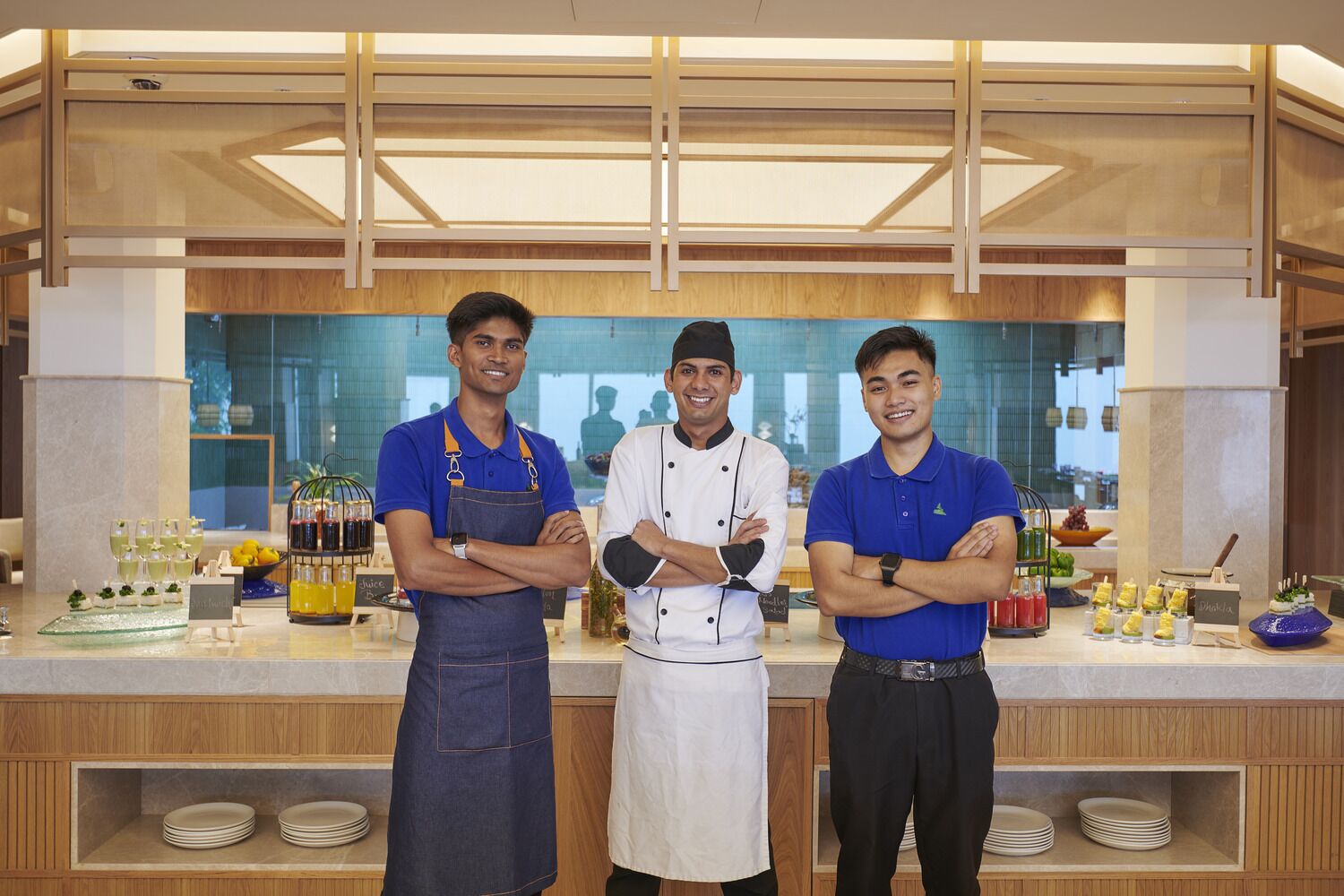 Tres empleados en un área de cocina moderna con paneles de madera y una división de vidrio.