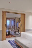 A hotel room with a bed, a desk, a chair, and a view of the balcony.