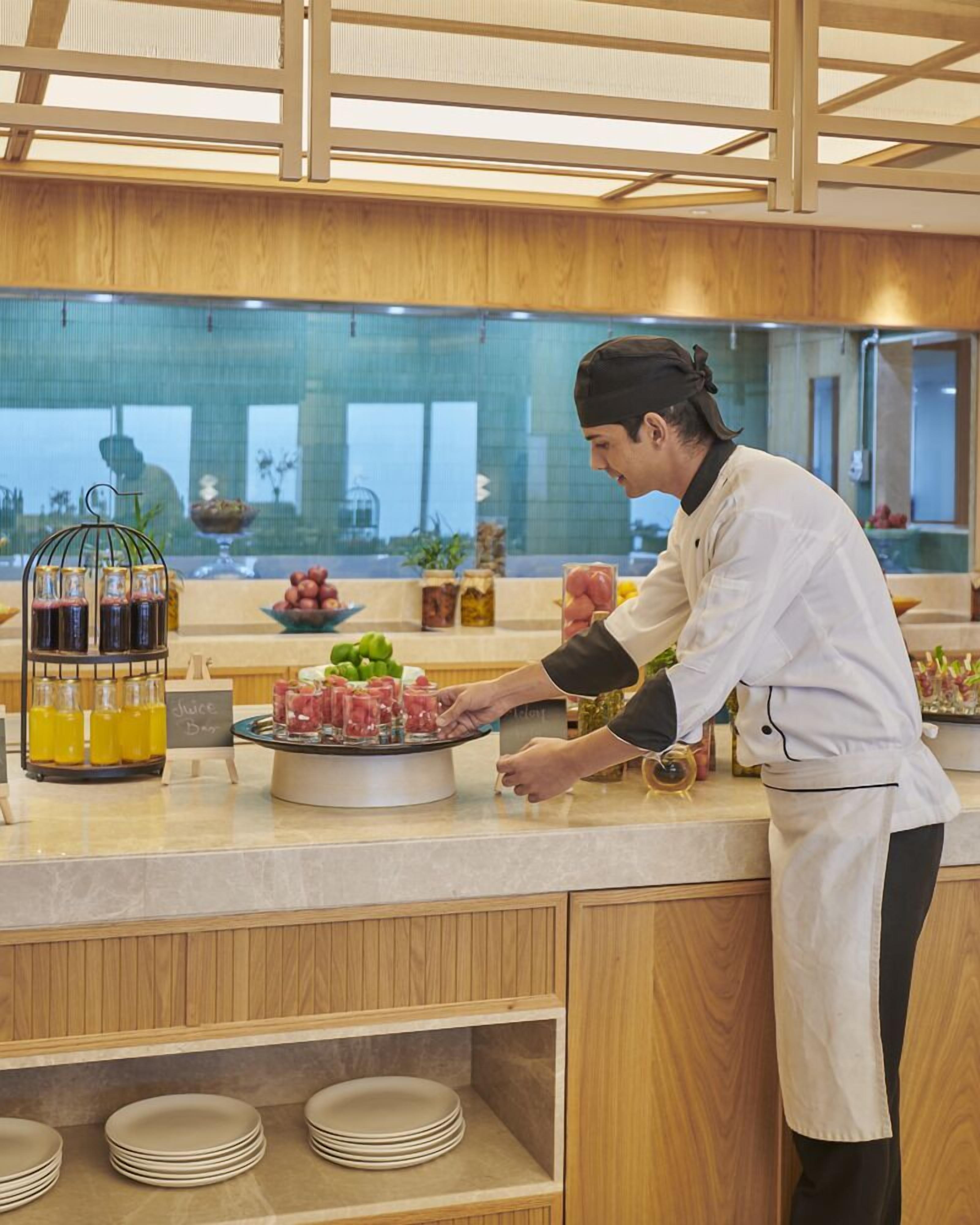 A chef preparing food at a buffet counter with a variety of dishes and condiments.