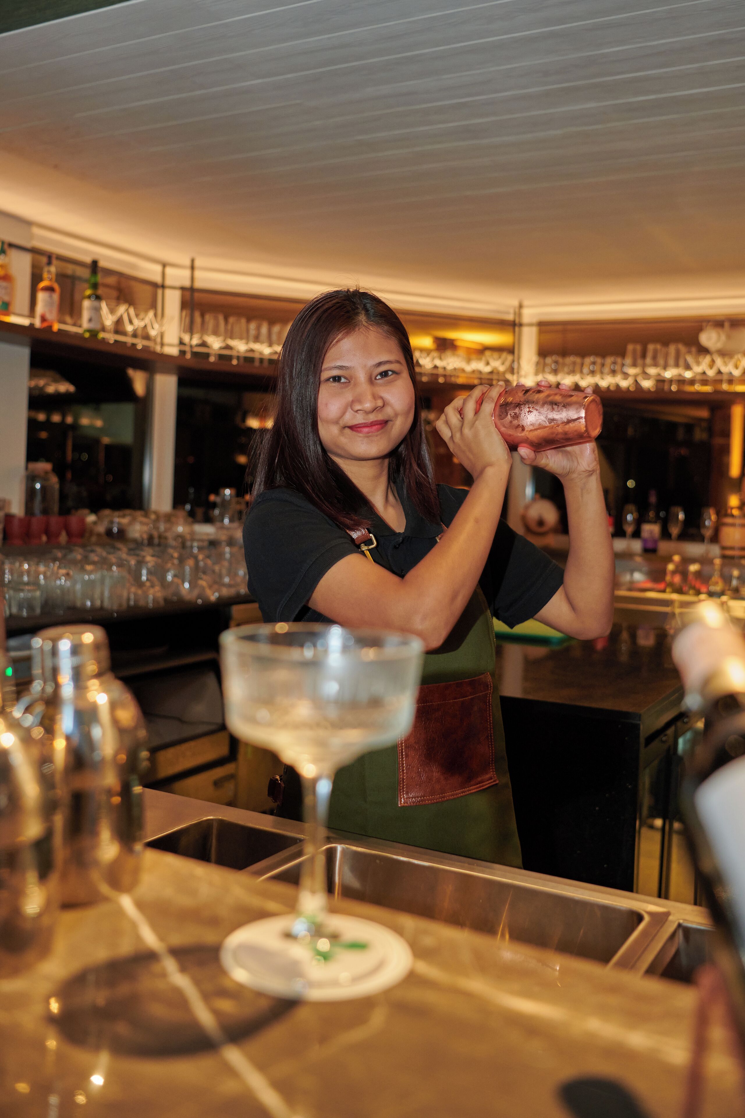 A bartender preparing a drink behind a bar with glasses and bottles.