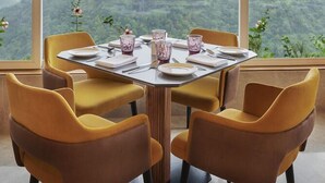 A dining area with a round table set for four, large windows offering a view of a mountainous landscape. - Athiva Resort & Spa, Khandala (Mawal)
