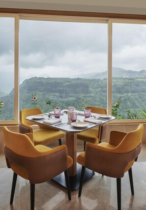 Un comedor con una mesa redonda dispuesta para cuatro personas, con ventanas amplias que ofrecen vistas a un paisaje montañoso.