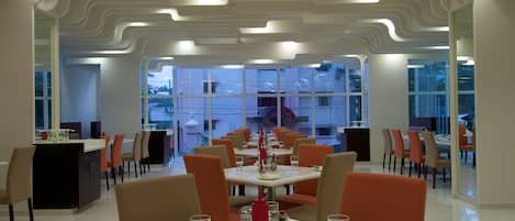A modern dining area with white tables, orange chairs, and a unique ceiling design.
