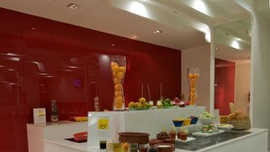 A modern kitchen with a central island, red cabinets, and various food items displayed on the counter. - Keys Select by Lemon Tree Hotels, Thiruvananthapuram (Thiruvananthapuram)