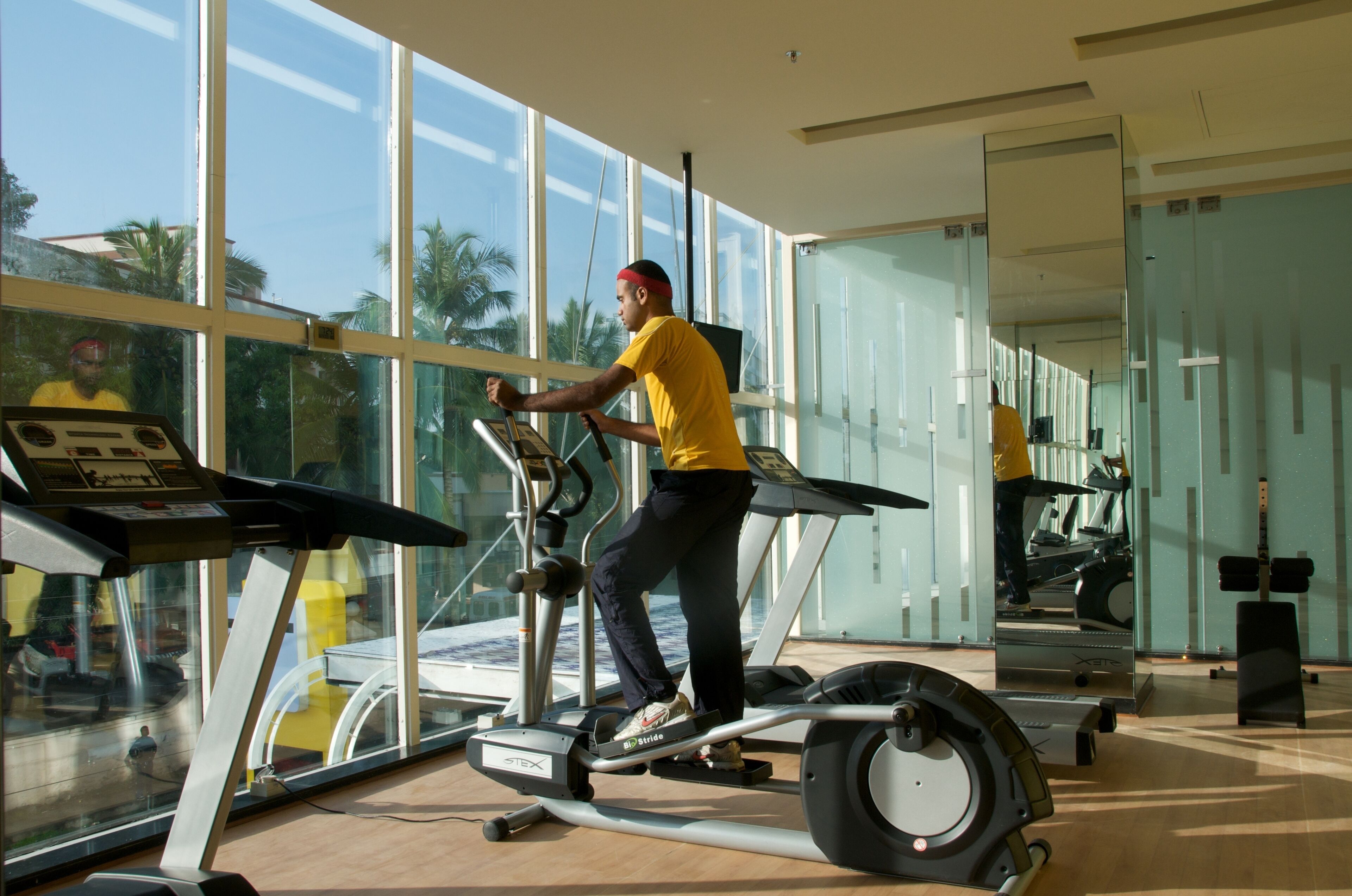 Une salle de sport dotée de grandes fenêtres, d’appareils d’exercice et d’un mur recouvert de miroirs.