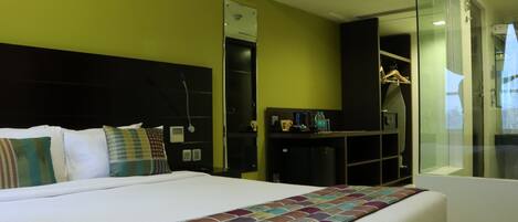 Habitación de hotel con una cama grande, un armario, un escritorio con silla y cabina de ducha de vidrio.