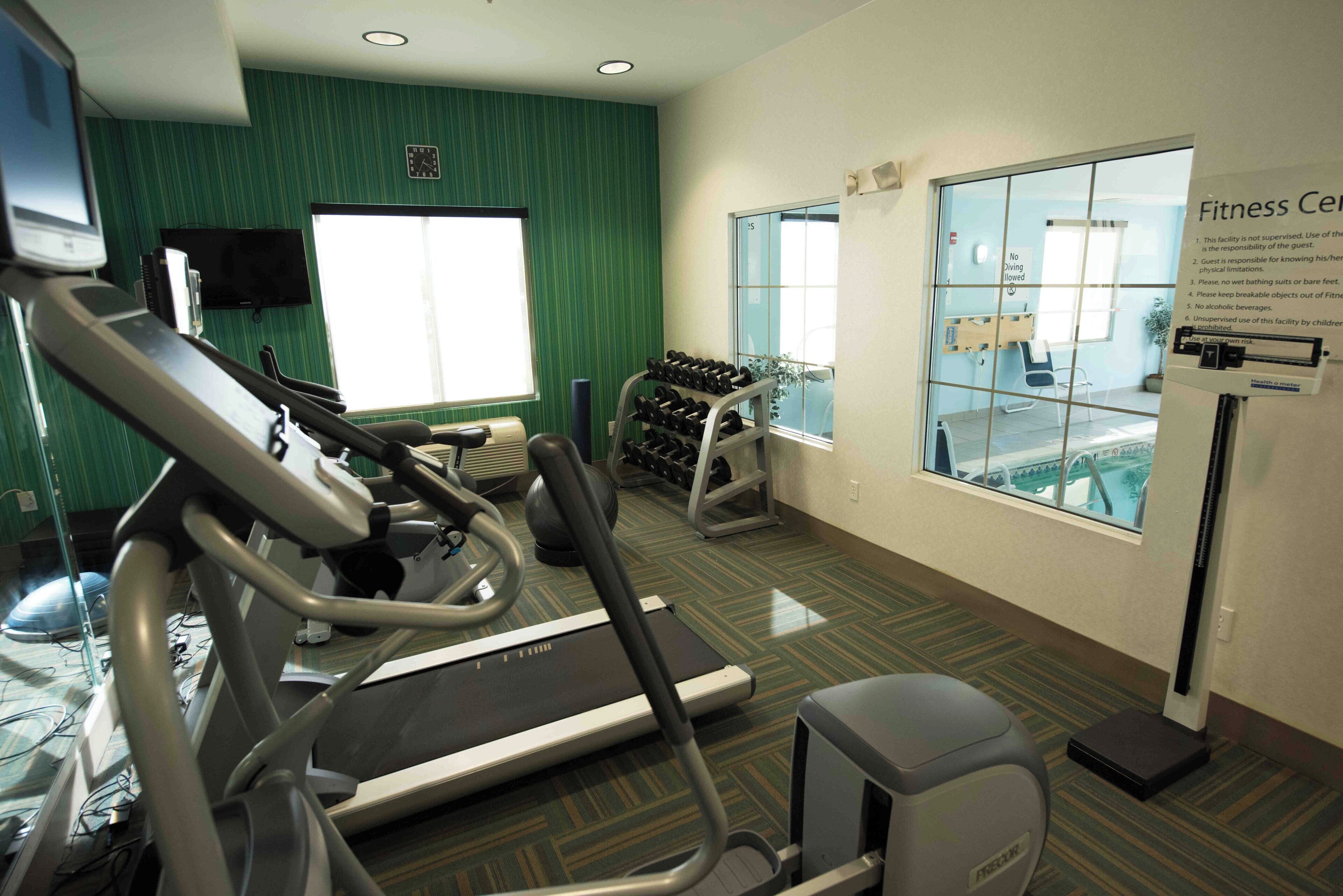 Een fitnessruimte met loopbanden, een tv aan de muur en een raam met uitzicht op een zwembad.
