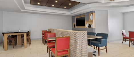 A modern dining area with wooden tables and chairs, a patterned partition, and a flat-screen TV mounted on the wall.
