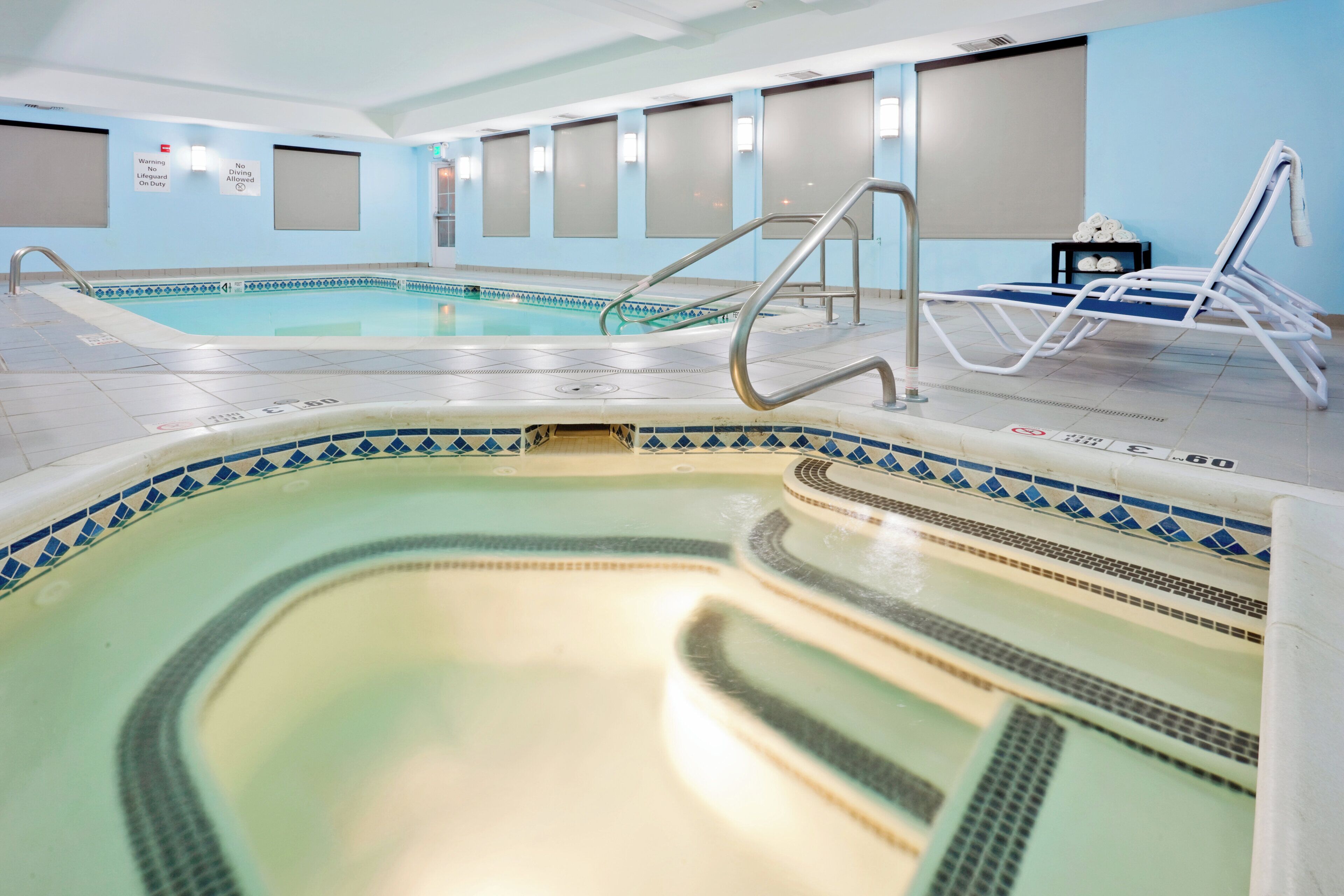 Una piscina interior con varias pistas de natación, un trampolín y sillas de descanso.